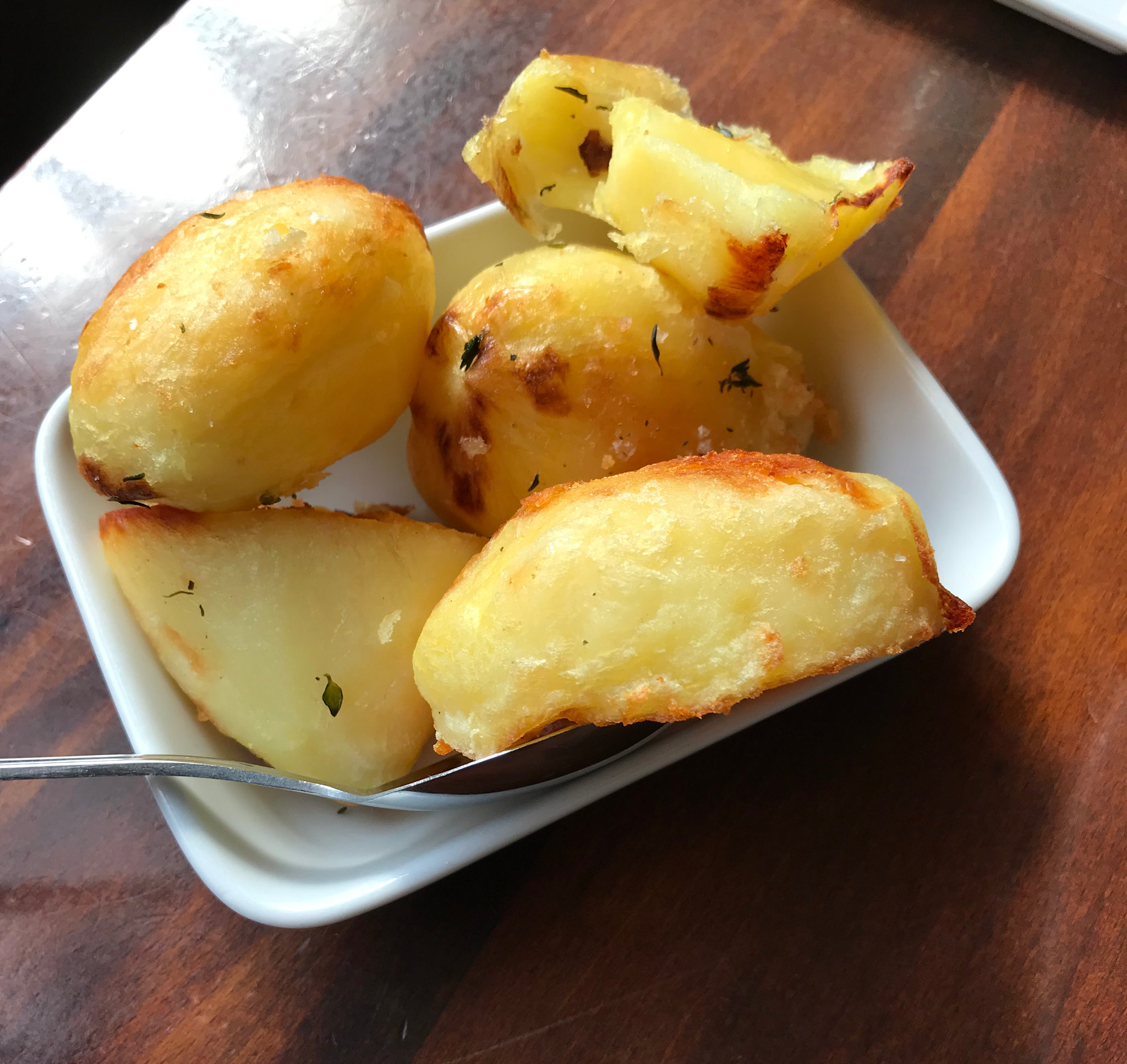 Close-up of roast potatoes in a white bowl, with one potato broken open to show the fluffy centre and crisp golden edge.